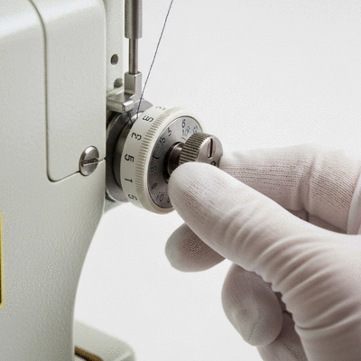 Close-up of a sewing machine tension dial being adjusted with a gloved hand, focus on precision and control, no text, no words, no typography, no labels, clean image